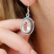 Close-up of a silver earring with a clear gemstone held by a hand.